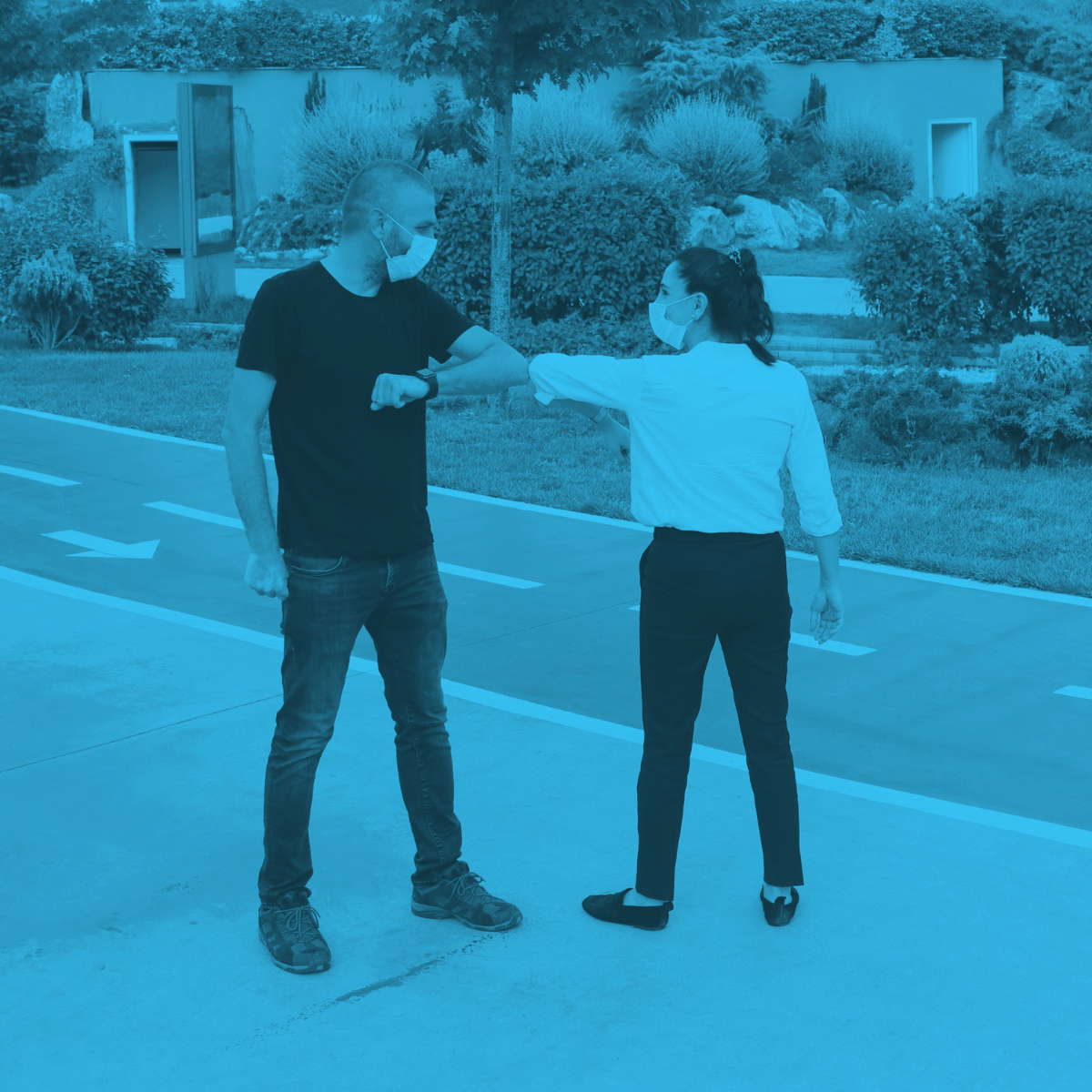 A man and a woman in face masks elbow bumping on a sidewalk with a teal filter overlay
